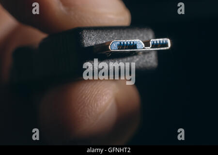 Hand holding black micro USB 3.0 cable. Man's hand holds a USB Connector. Closeup man hand holding USB cable. Stock Photo