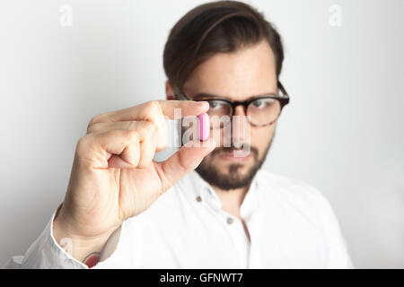 Young Bearded Man Wearing White Shirt Glasses Holding Pink Color Pill.Medicine Health Care People Concept Photo.Adult Serious Doctor Empty Background.Horizontal. Stock Photo