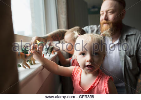 Portrait daughter and father playing with toy dinosaurs at windowsill Portrait daughter and father playing with toy dinosaurs at windowsill