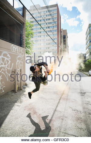 Cool young man doing parkour backflipping with powder cannon in urban alley
