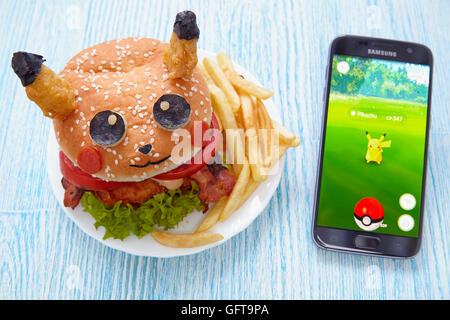 Moscow, Russia - July 29, 2016 Editorial image: Fan Art Pikachu Burger and Smartphone with Pokemon Go application. Selective foc Stock Photo