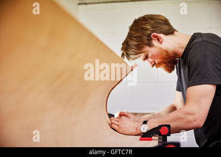 A  man using a tool on the curved cut out edge of a piece of wood Stock Photo