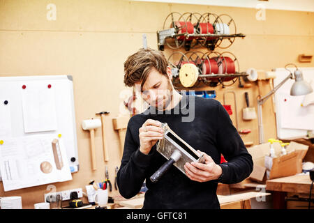 A furniture workshop  A young man holding an object and examining it closely Stock Photo