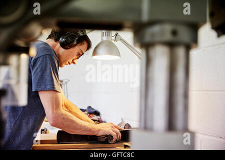 A furniture workshop ,A man in ear defenders holding wood using a machine Stock Photo