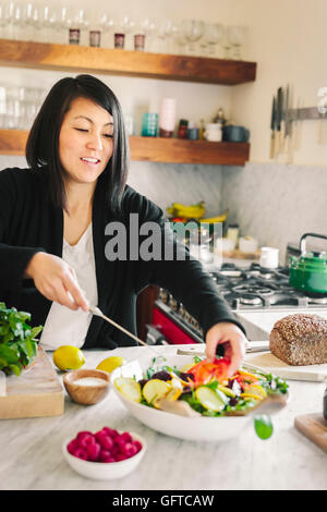 A woman in a kitchen preparing a salad dish with fresh vegetables Stock Photo