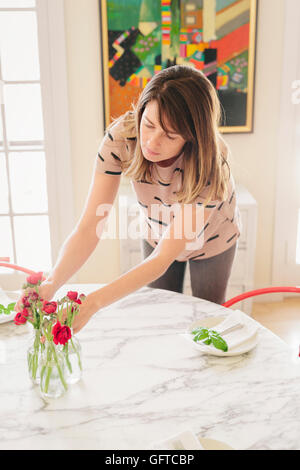 A woman arranging fresh cut flowers in the centre of a table Stock Photo