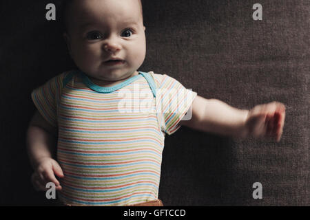 A six month old baby girl on a stripey vest lying on her back Stock Photo