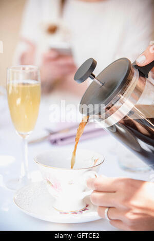 Close up of coffee being poured from a French Coffee  Press into a cup a glass of champagne Stock Photo