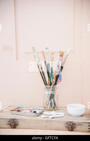 Painting materials glass jar with paint brushes paint tubes and a bowl Stock Photo