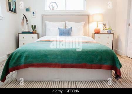 A green fabric quilt with red trim over a double bed in a light airy apartment Stock Photo