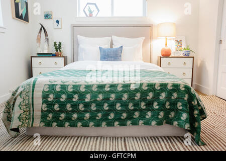 A bedroom in an apartment with a double bed and beside cabinets and a green fabric patterned bedspread Stock Photo