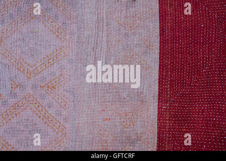 Full frame view of an antique bedspread patterned fabric with a faded strip and a red border with small running stitches Stock Photo