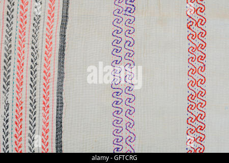 Full frame view of vintage fabric embroidered with a scrolling pattern in red and purple green and orange on a pale background Stock Photo