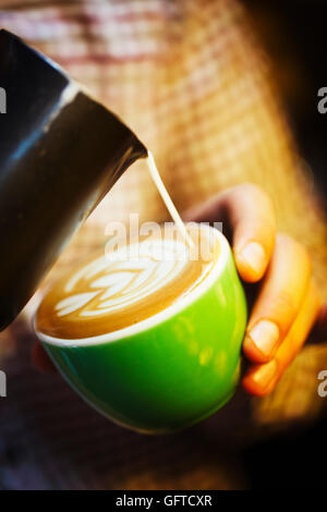 A barista creating a pattern in the froth on a cup of coffee Stock Photo
