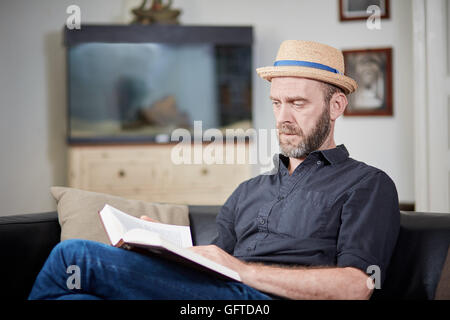 Man with beard and hat reads a book at home in an old building Stock Photo