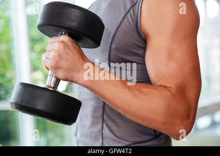 Closeup of athletic young man athlete training using dumbbells in gym Stock Photo