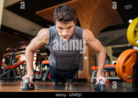 Strong young man athlete training and doing push-ups in gym Stock Photo