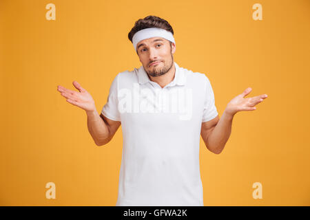 Confused handsome young sportsman standing and shrugging shoulders over yellow background Stock Photo