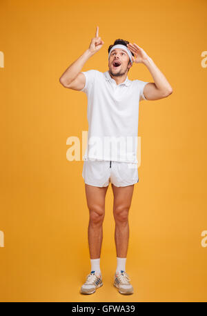 Full length of surprised young sportsman looking and pointing up over yellow background Stock Photo