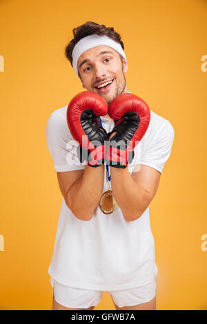 Happy cute young man boxer in red gloves making heart by hands over yellow background Stock Photo