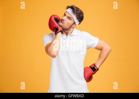 Portrait of young man boxer in red gloves standing and warming up over yellow background Stock Photo
