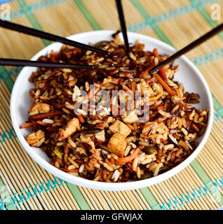 closeup of a white ceramic bowl with appetizing asian fried rice and some chopsticks, on a bamboo mat Stock Photo