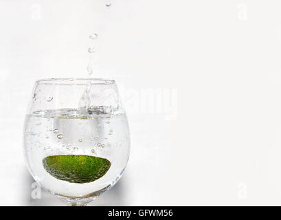 A piece of lime being dropped into a glass of fizzy drink on white background on left hand side Stock Photo