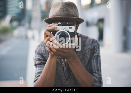 Half length of young beautiful afro black man outdoor in the city holding instant camera, shooting - photography, creative, artist concept Stock Photo