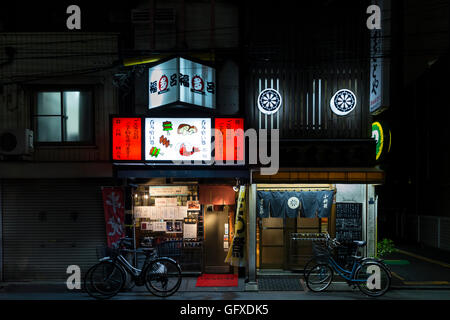 Single small restaurant with red illuminated advertising and bicycles close to Ueno train station in Tokyo, Japan Stock Photo