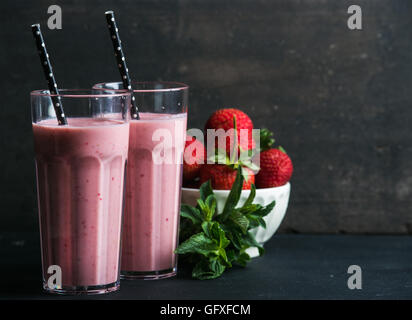 Strawberry and mint smoothie in tall glasses, bawl of fresh berries on dark rustic wood background Stock Photo