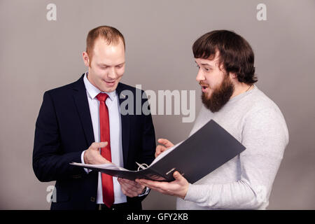 Two business people in elegant suits sitting at desk working in team together and discussing the problem holding clipboard, folder with papers, document, business plan. Isolated over white background. Stock Photo