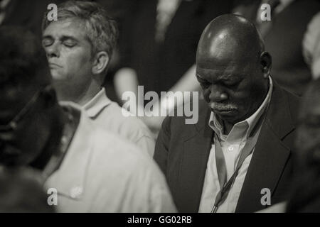 An african american / black man and caucasian / white man sit side by side in prayer at the 2016 democratic national convention held in Philadelphia PA at the Wells Fargo Center Stock Photo