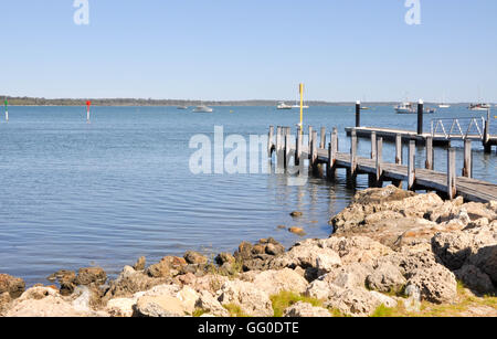 Mandurah foreshore with calm river, wooden jetty and dock with boats under a clear sky in Western Australia. Stock Photo