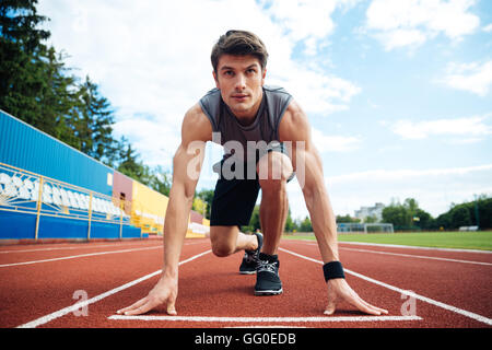 Young handsome man in starting position for running on sports track Stock Photo