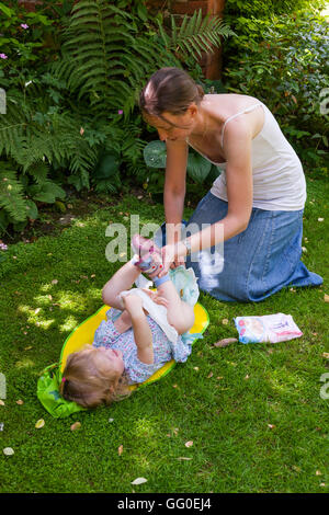 Mum mother parent carer changing nappies nappy change of baby toddler. Open air garden / outside / exterior / outdoors / outdoor Stock Photo