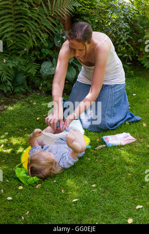 Mum mother parent carer changing nappies nappy change of baby toddler. Open air garden / outside / exterior / outdoors / outdoor Stock Photo