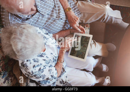 Top view of senior couple sitting together looking at pictures on digital tablet. Mature man and woman sitting on sofa looking i Stock Photo