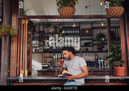 Handsome young man drinking coffee and reading book at a cafe. Stock Photo