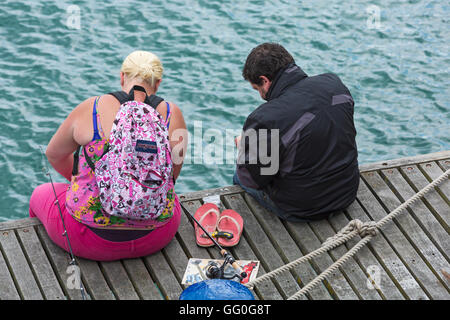 Looking down on man and woman sat down fishing at Swanage Pier in July Stock Photo