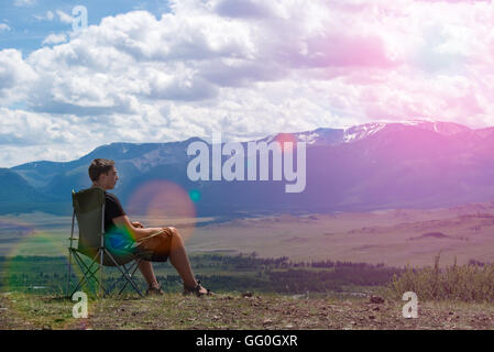 man sitting on a chair in the mountains and looks into the distance Stock Photo