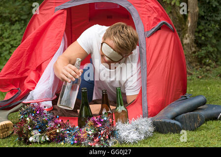 CAMPING PARTY TIME  - A young man reaches outside a tent for a water bottle Stock Photo