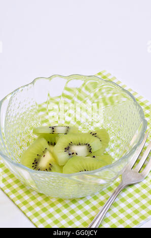 sliced kiwi fruit in a bowl on white and light green checkered napkin, macro, close up, white background, space for text Stock Photo