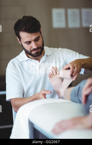 Physiotherapist putting bandage on injured feet of patient Stock Photo