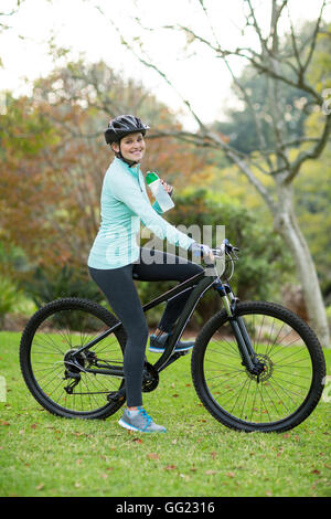 Beautiful female cyclist drinking water in forest Stock Photo