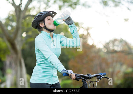 Female cyclist drinking water in forest Stock Photo