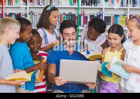 Teacher teaching kids on laptop in library Stock Photo