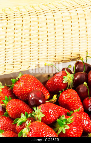 Strawberries and cherries in a wicker basket in the background. Vertical image. Stock Photo