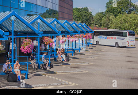 National Express coach at Bournemouth Coach Station, Bournemouth, Dorset UK with people waiting and colourful hanging baskets in July - hdr effect Stock Photo