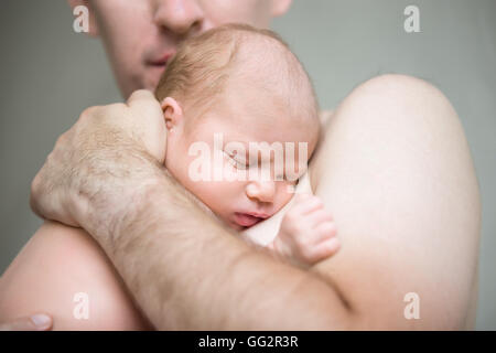 Young happy man holding his sleeping newborn cute babe. Newborn babe sleeping in male hands. Healthy little kid after birth Stock Photo