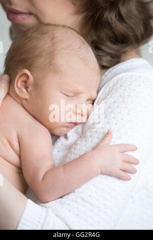 Portrait of young mother tenderly embracing sleeping cute new born child. Funny newborn babe napping in mom arms Stock Photo